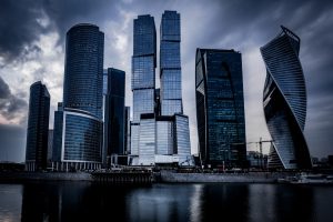 low-angle-shot-grey-skyscrapers-front-river-dark-cloudy-sky (1)